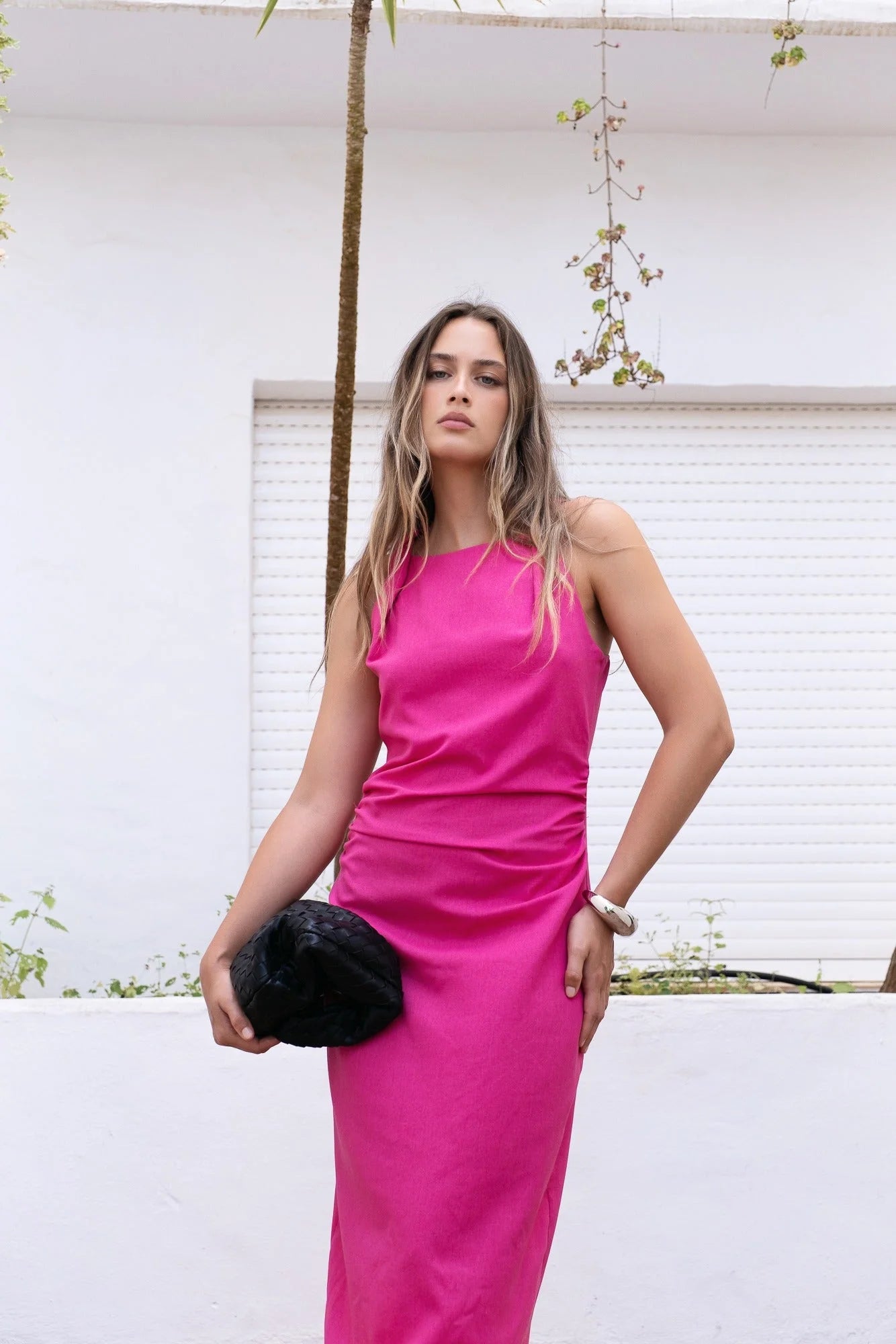 Robe fuchsia longue sans manches avec fronces, clutch noir et bracelet argenté