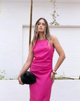 Femme prenant la pose avec une robe fuchsia longue chic en lin, sans manches, encolure froncée, style minimaliste, devant une arrière-plan naturel.