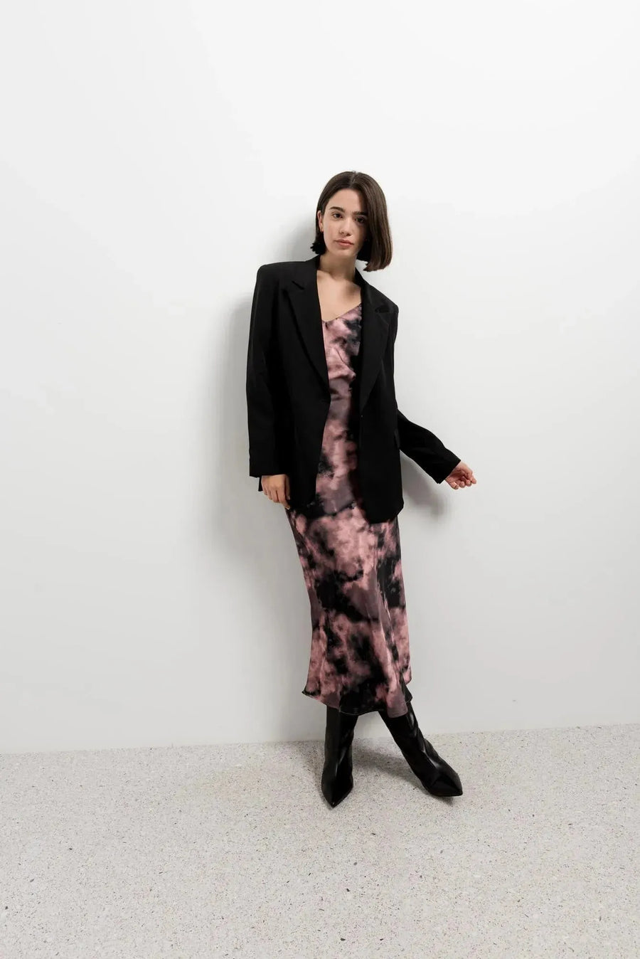 Femme stylée avec une robe tie dye longue satinée noir et rose sous un blazer, parfaite pour une soirée.