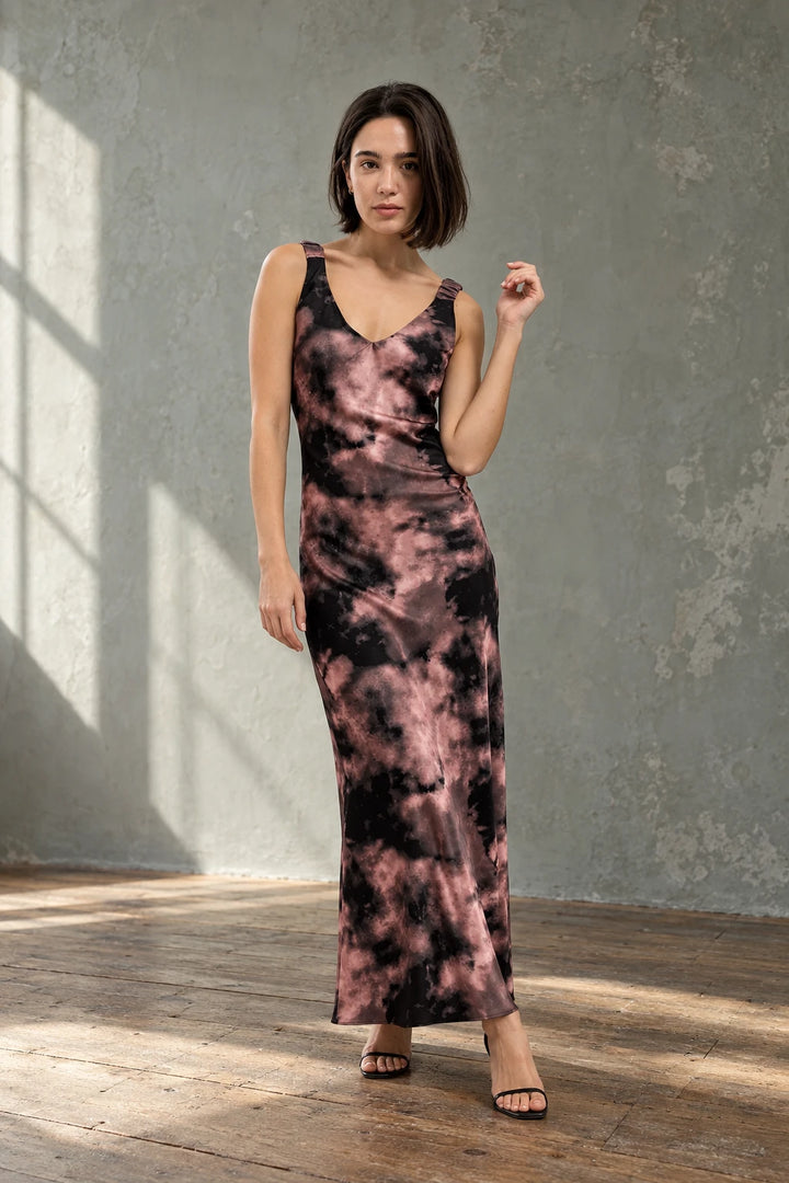 Modèle portant une robe tie dye longue satinée noir et rose, imprimé effet nuage, col en V, bretelles larges.