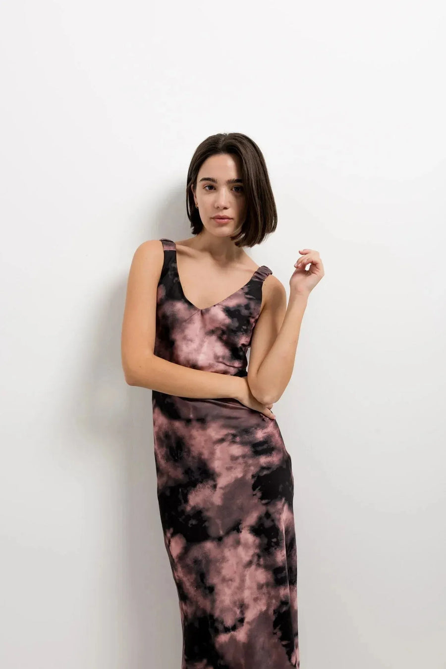 Modèle portant une robe tie dye longue satinée noir et rose, imprimé effet nuage, col en V, bretelles larges.