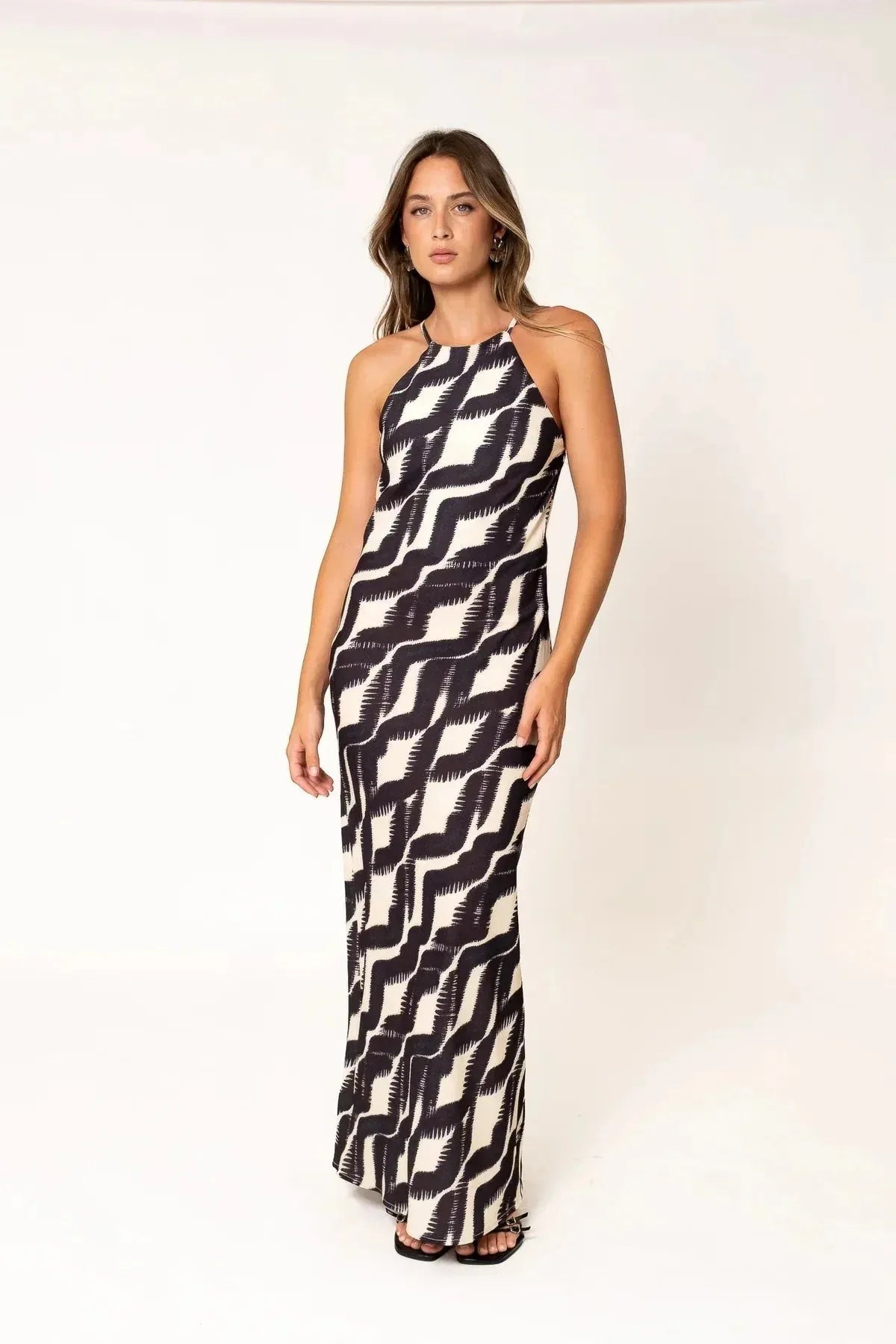 Robe Longue Col Halter Imprimée Graphique Noir et Beige – Élégance Estivale. Mannequin portant la robe longue col halter devant un fond neutre, la silhouette mise en valeur.