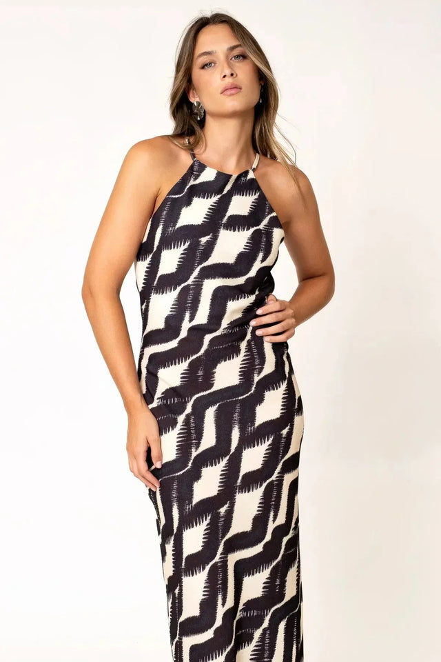 Robe Longue Col Halter Imprimée Graphique Noir et Beige – Élégance Estivale. Modèle féminine stylée posant dans une robe longue col halter, le design unique au premier plan.