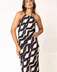 Robe Longue Col Halter Imprimée Graphique Noir et Beige – Élégance Estivale. Modèle féminine stylée posant dans une robe longue col halter, le design unique au premier plan.