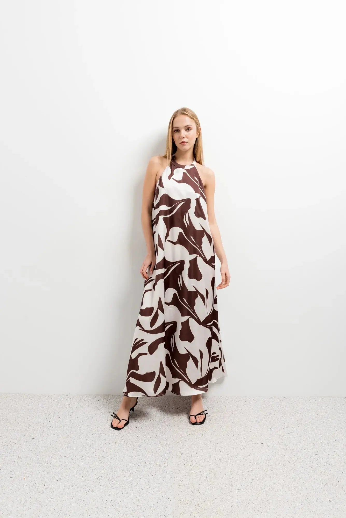 Robe Longue Bohême Imprimée Chocolat & Blanc Dos Nu Fluide avec Col Licou, modèle devant un fond neutre, mettant en avant le motif original et le style chic.