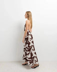 Robe Longue Bohême Imprimée Chocolat & Blanc Dos Nu Fluide avec Col Licou, femme de profil dans un décor minimaliste, mettant en avant le design élégant.