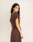 Robe longue marron ajustée femme avec détails drapés, modèle regardant au-dessus de son épaule.