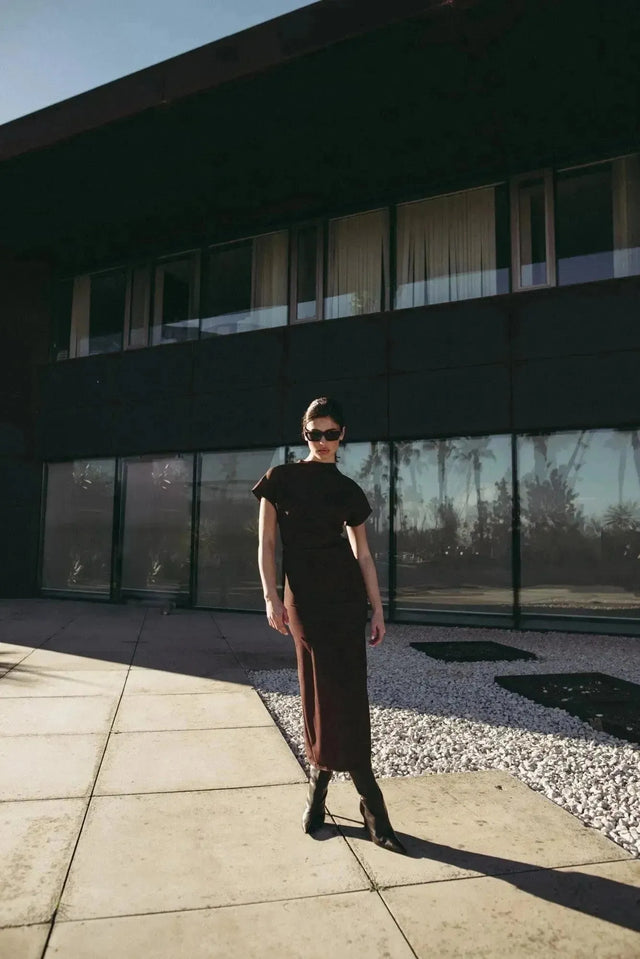 Robe longue marron ajustée femme avec détails drapés, modèle posant à l'extérieur avec des lunettes de soleil.