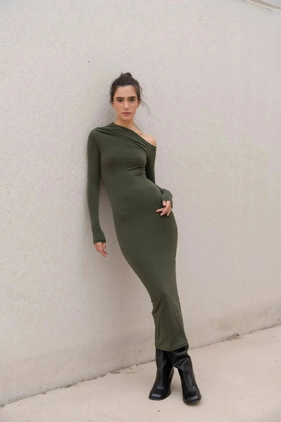 Modèle portant une robe moulante kaki femme à épaule dénudée contre un mur, mettant en valeur la coupe asymétrique de la robe moulante kaki.