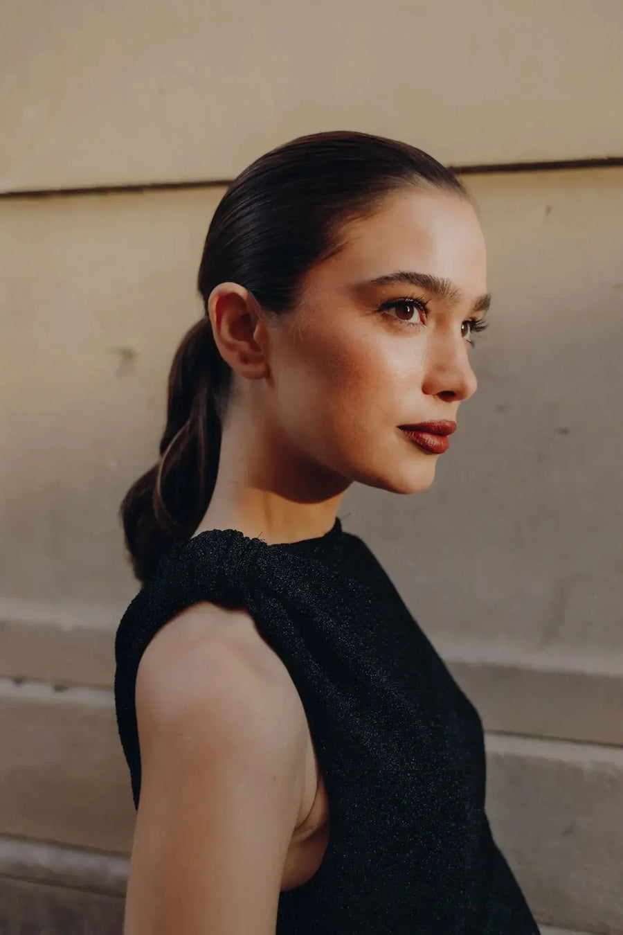 Gros plan sur le visage d'une femme portant une robe longue noire ajustée sans manches avec nœud, mettant en avant ses traits et le tissu sophistiqué.