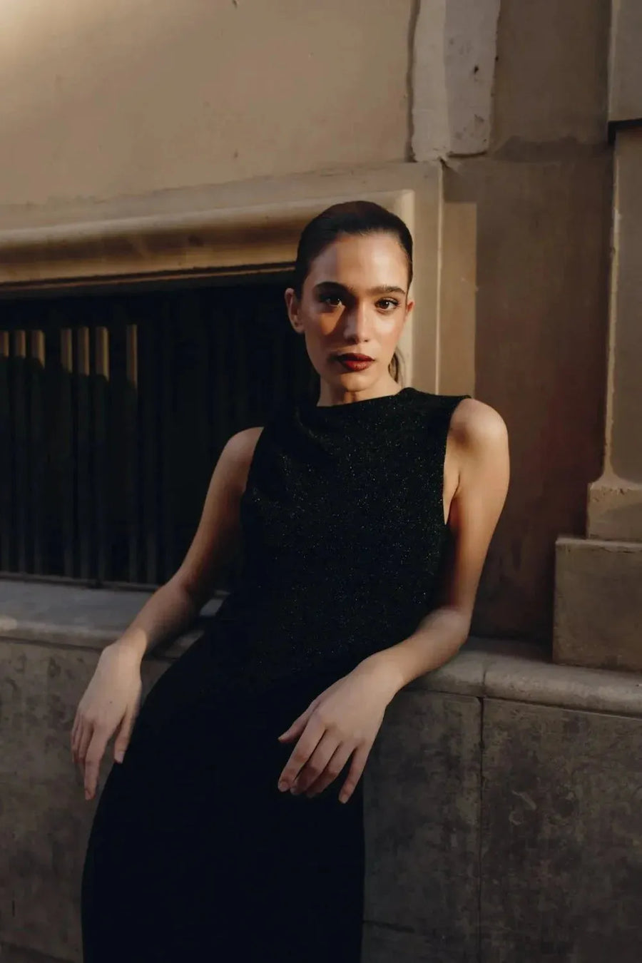 Femme affichant une attitude confiante dans une robe longue noire ajustée sans manches avec nœud, accentuant son élégance minimaliste.