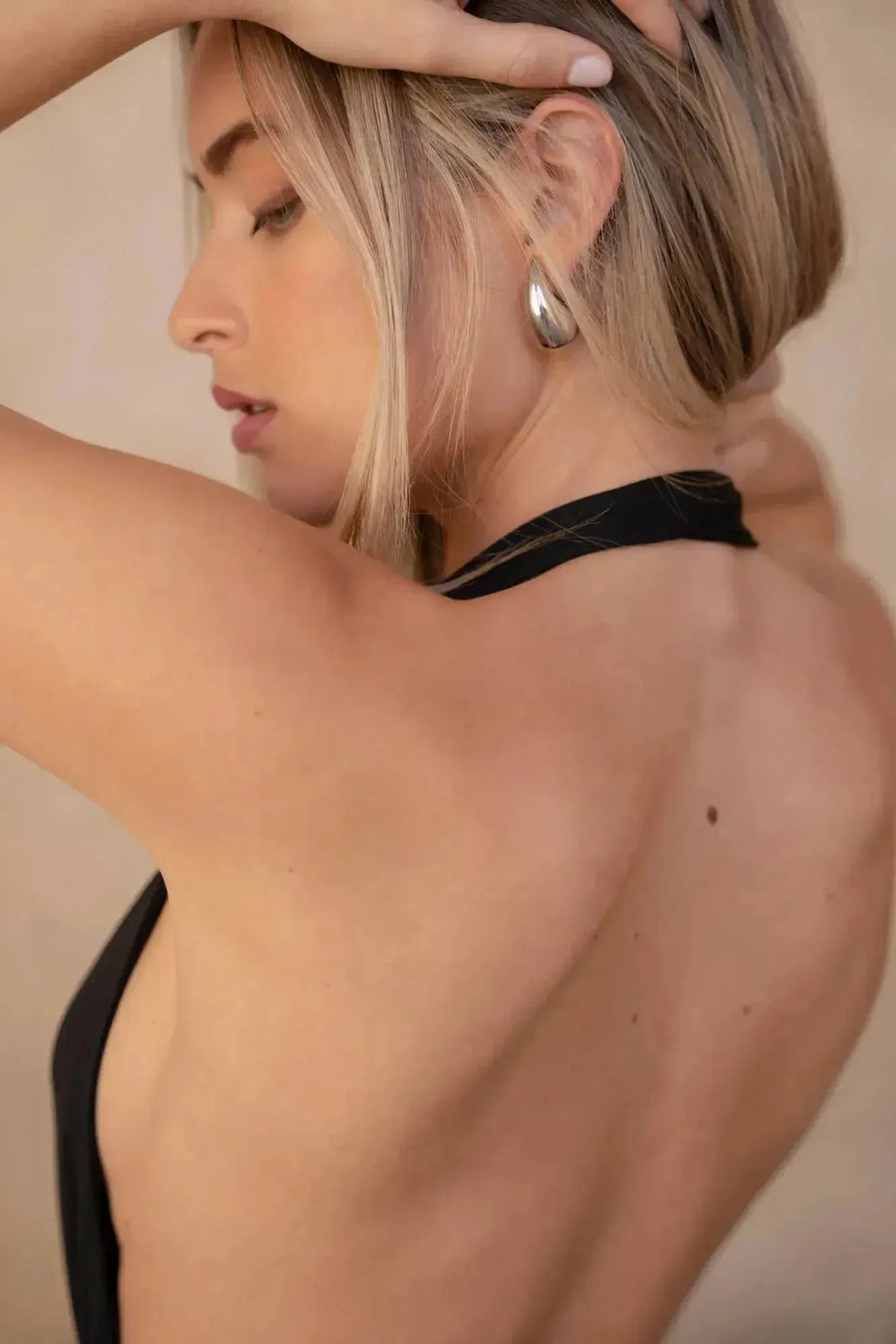 Profil d'une modèle mettant en valeur le dos nu de la robe longue noire, ajoutant une allure sophistiquée. Parfaite comme robe longue pour mariage invité chic.