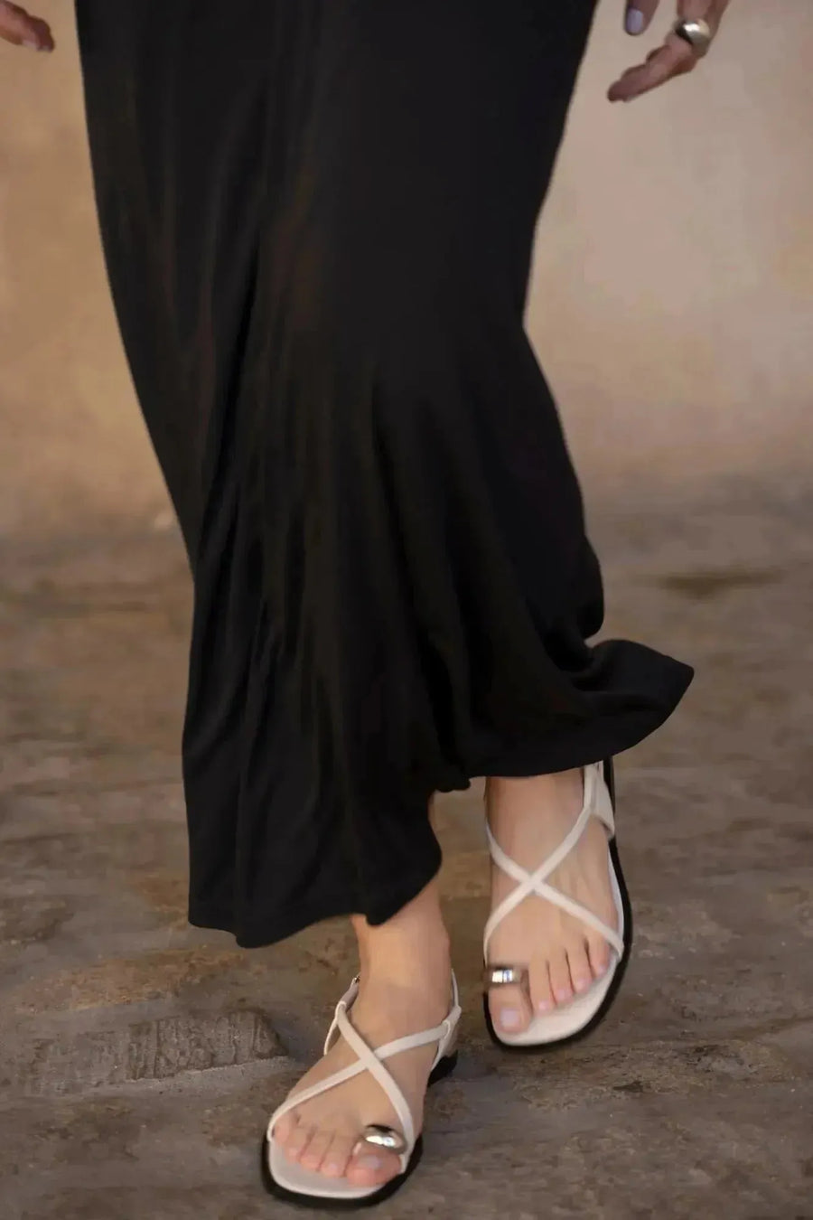 Modèle en gros plan des pieds portant des sandales sous la robe longue noire dos nu, ajoutant une touche de style. Une option chic pour robe longue pour mariage invité.