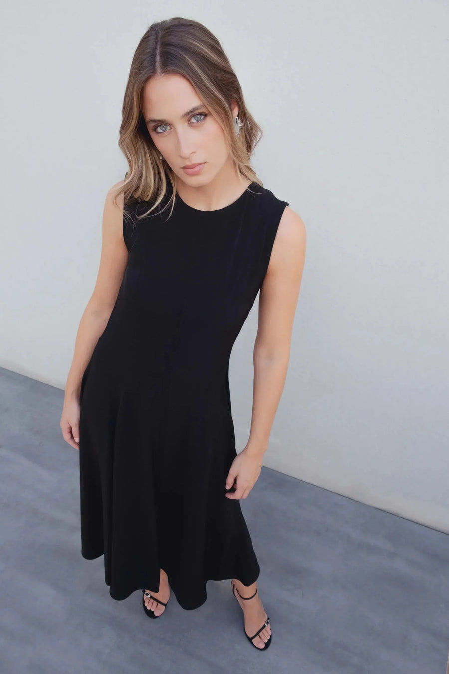 Robe Longue Noire Élégante Sans Manches - Coupe Midi, Ourlet Festonné, Col Rond, photographiée sous un angle créatif, mettant en valeur le mouvement et le style moderne.