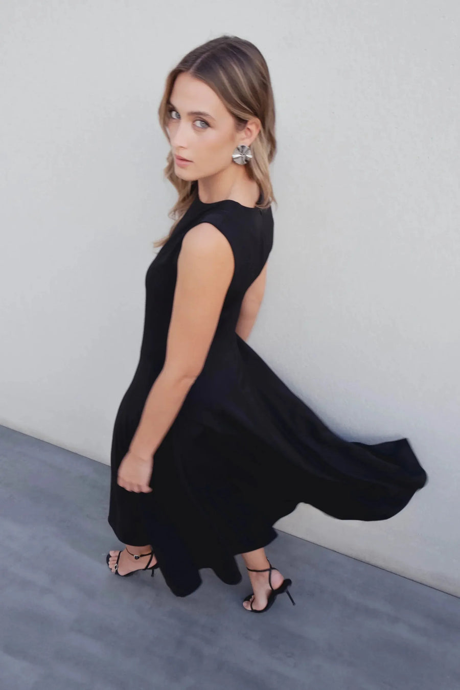 Robe Longue Noire Élégante Sans Manches - Coupe Midi, Ourlet Festonné, Col Rond, en action, illustrant la fluidité et le design chic.