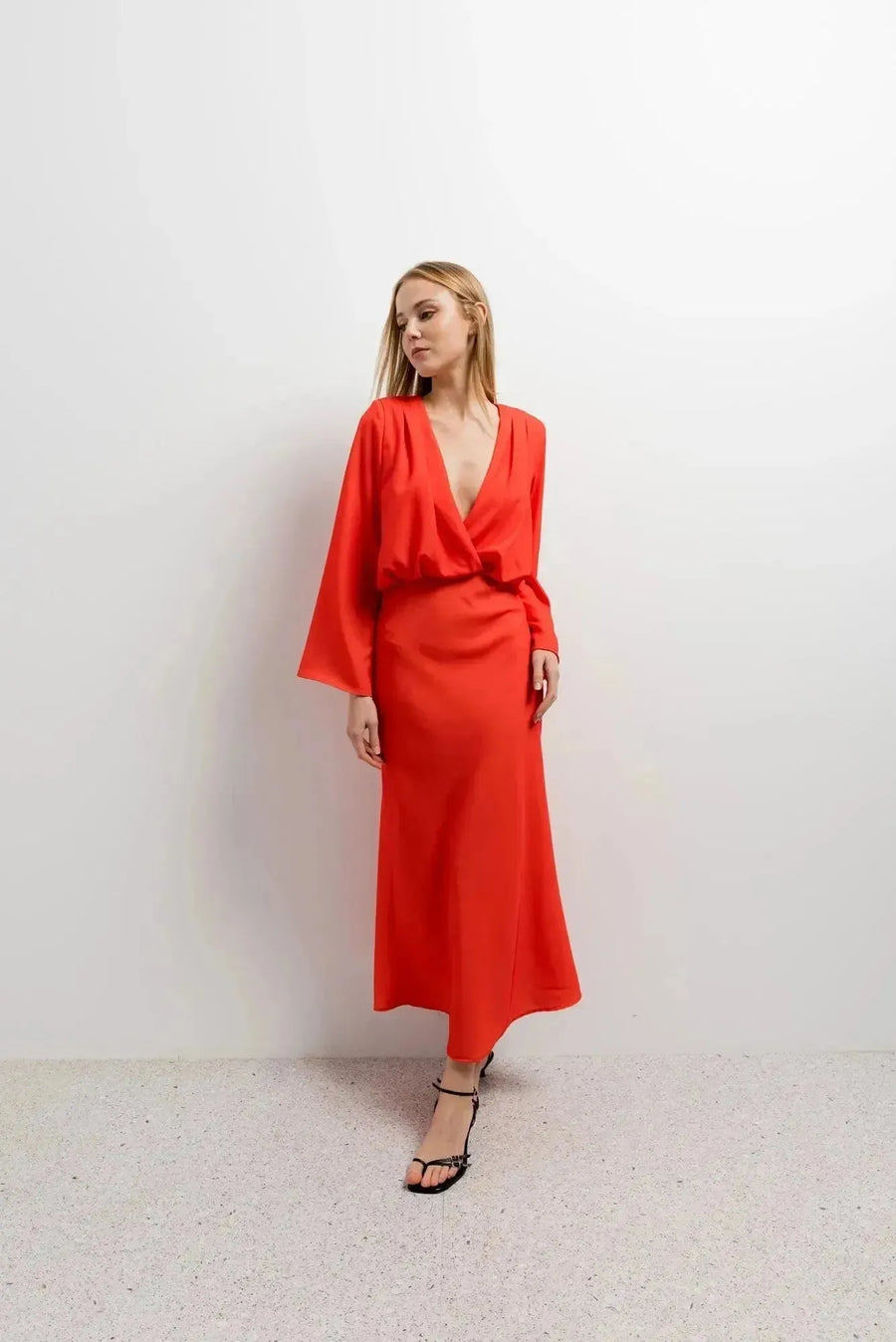 Femme en robe satinée rouge midi croisée avec décolleté plongeant, posant devant un fond blanc.