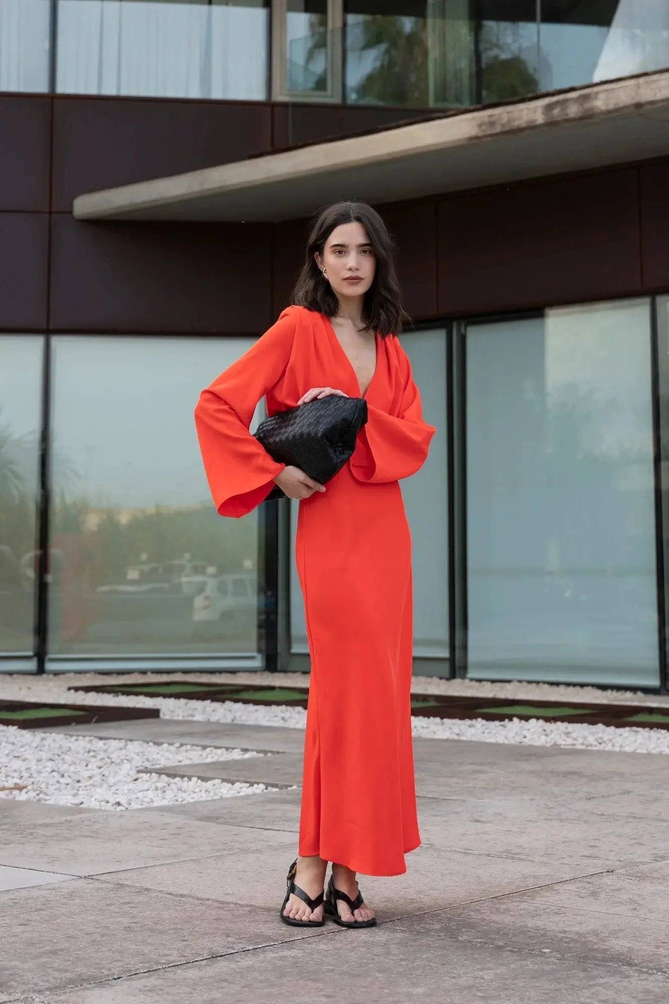 Femme en robe rouge satinée croisée avec manches larges, clutch noir et sandales noires
