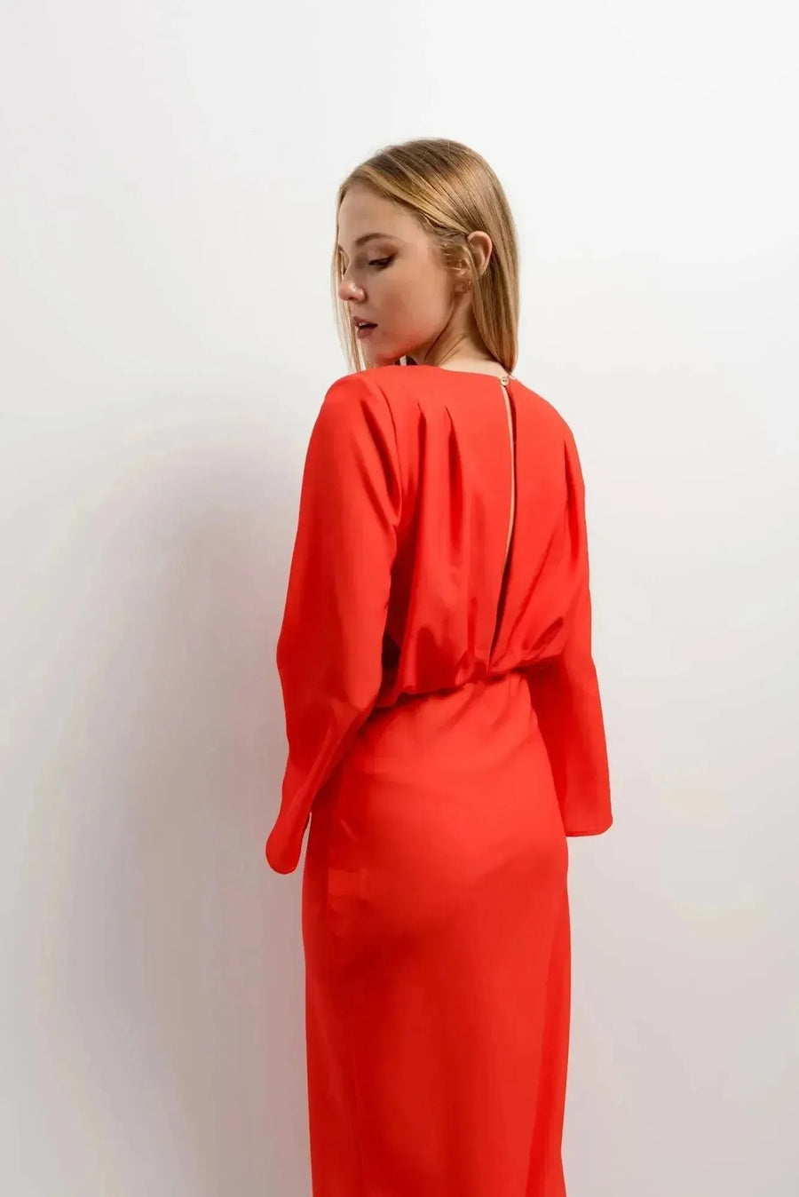 Vue arrière d'une femme dans une robe satinée rouge midi croisée avec décolleté plongeant, mettant en valeur la coupe et le tissu.