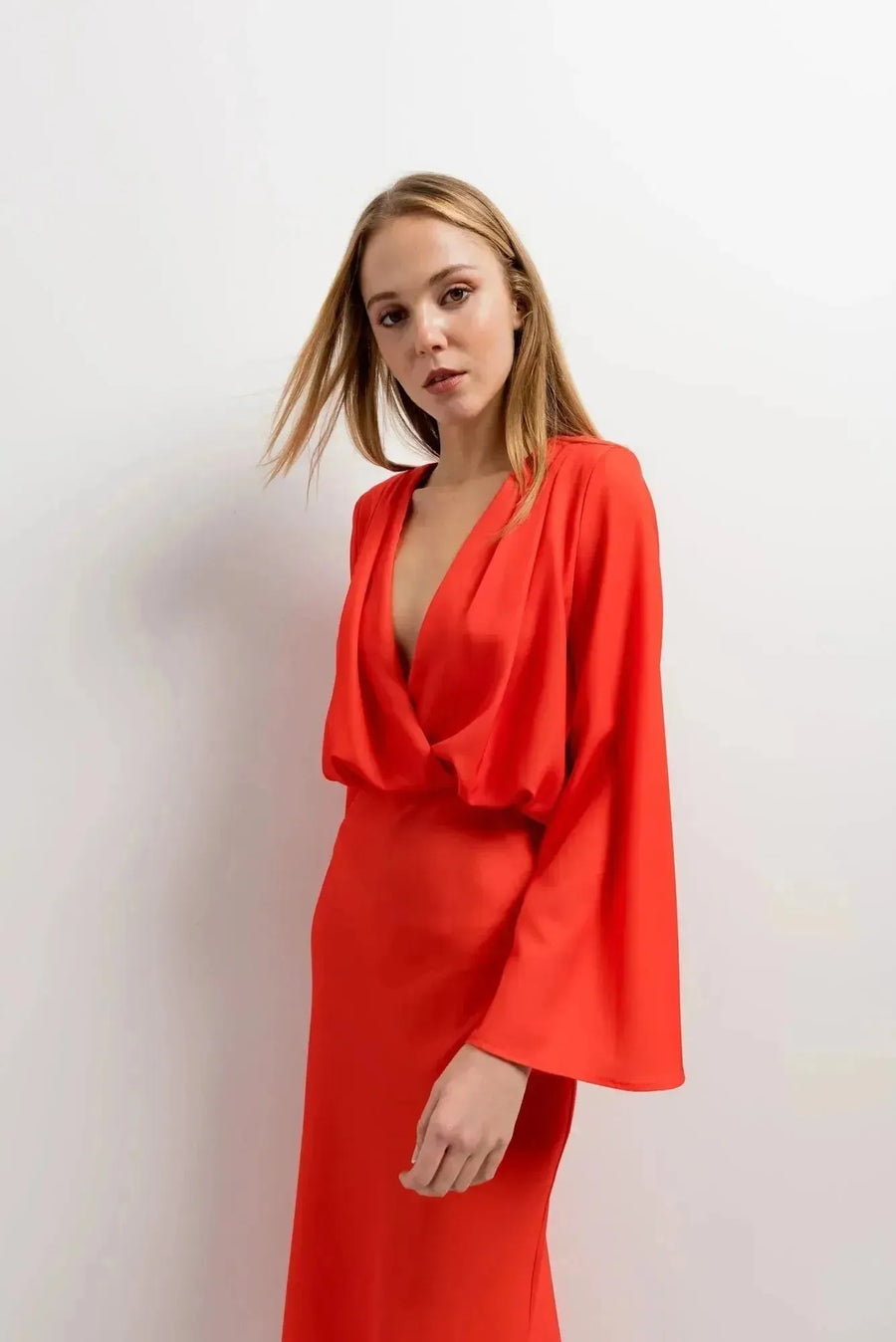 Portrait d'une femme portant une robe satinée rouge midi croisée avec décolleté plongeant, en pleine pose.