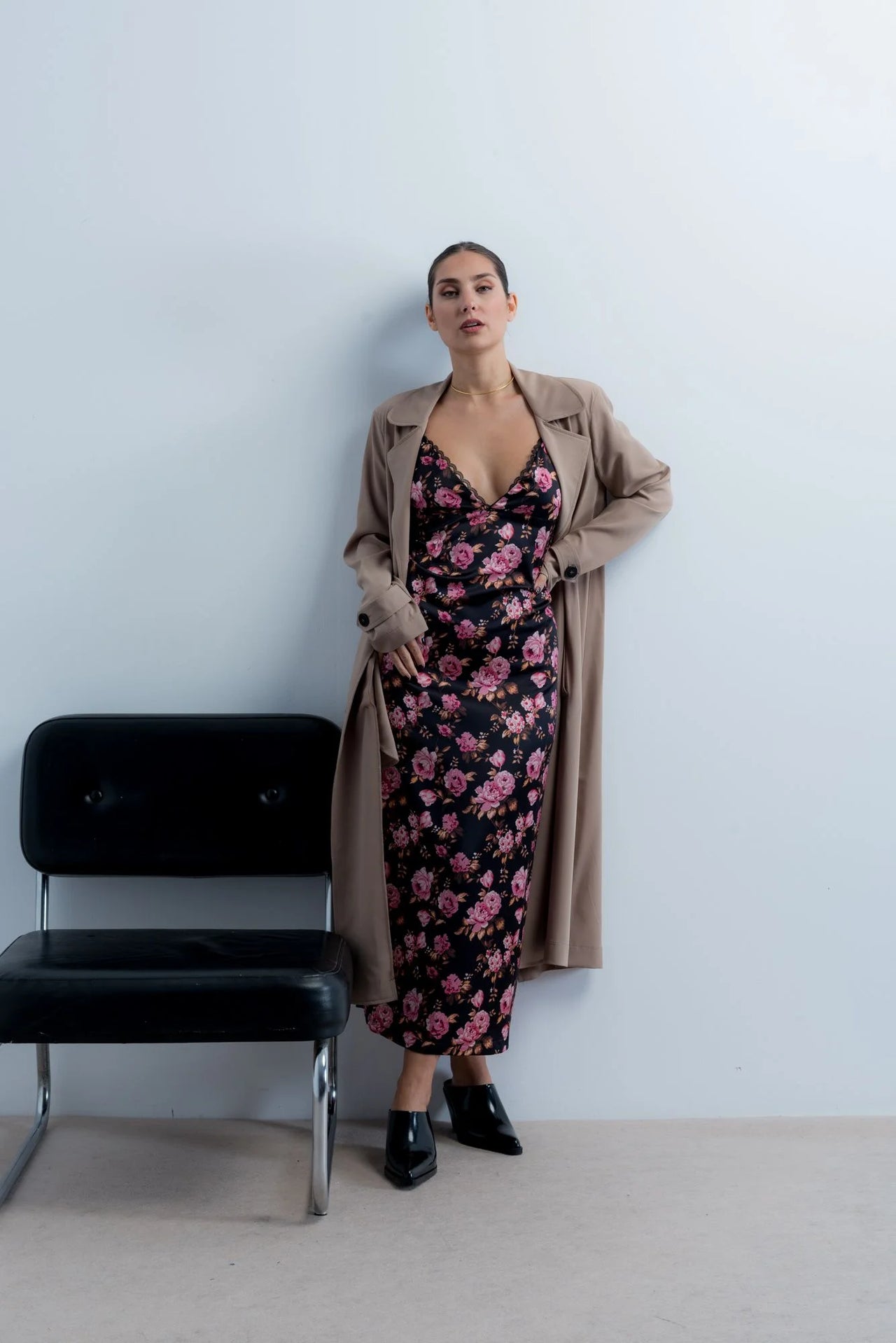 Femme portant une robe longue satinée noire à fleurs roses et trench beige