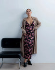 Femme portant une robe longue satinée noire à fleurs roses et trench beige
