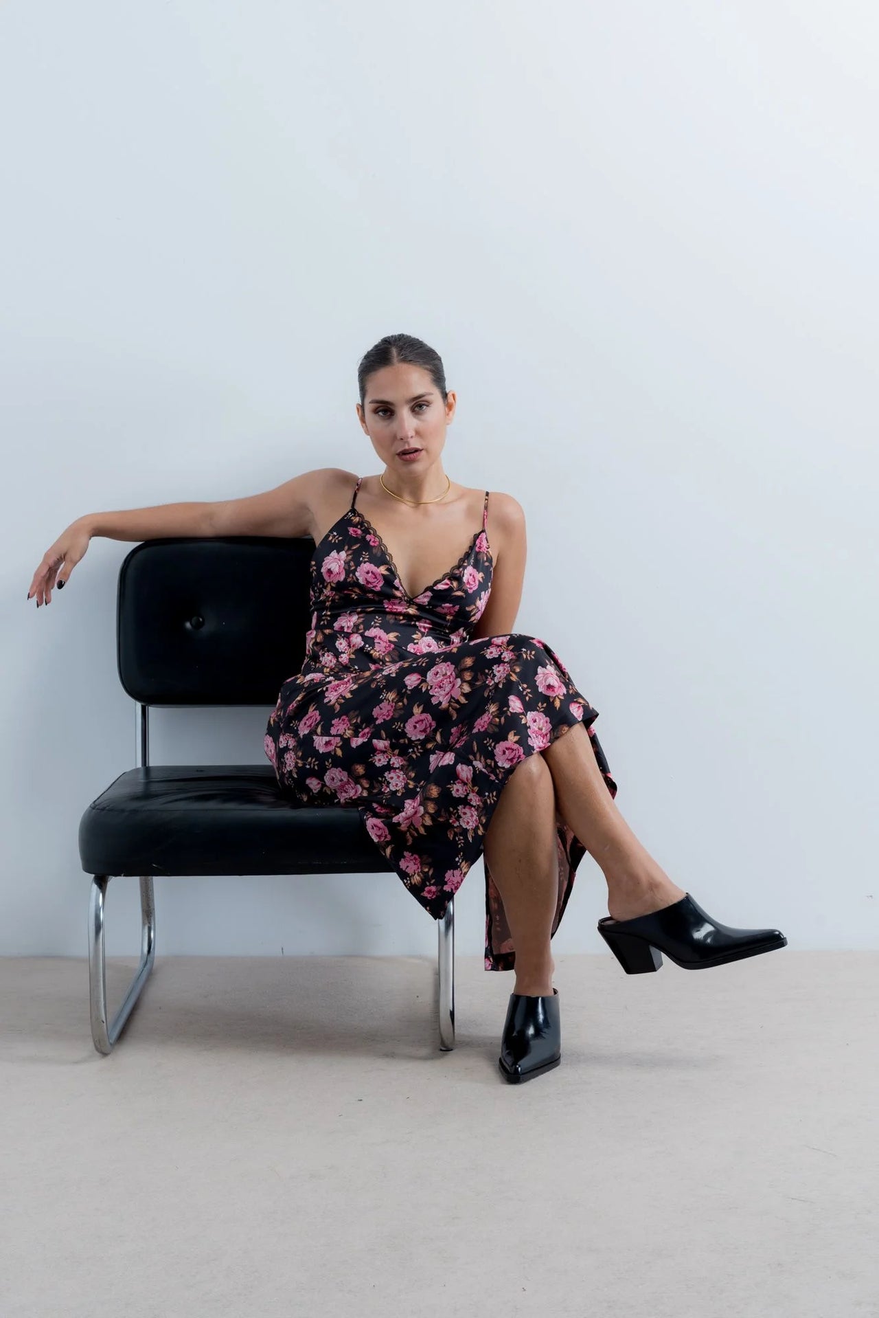 Femme portant une robe longue satinée noire à fleurs roses et mules noires