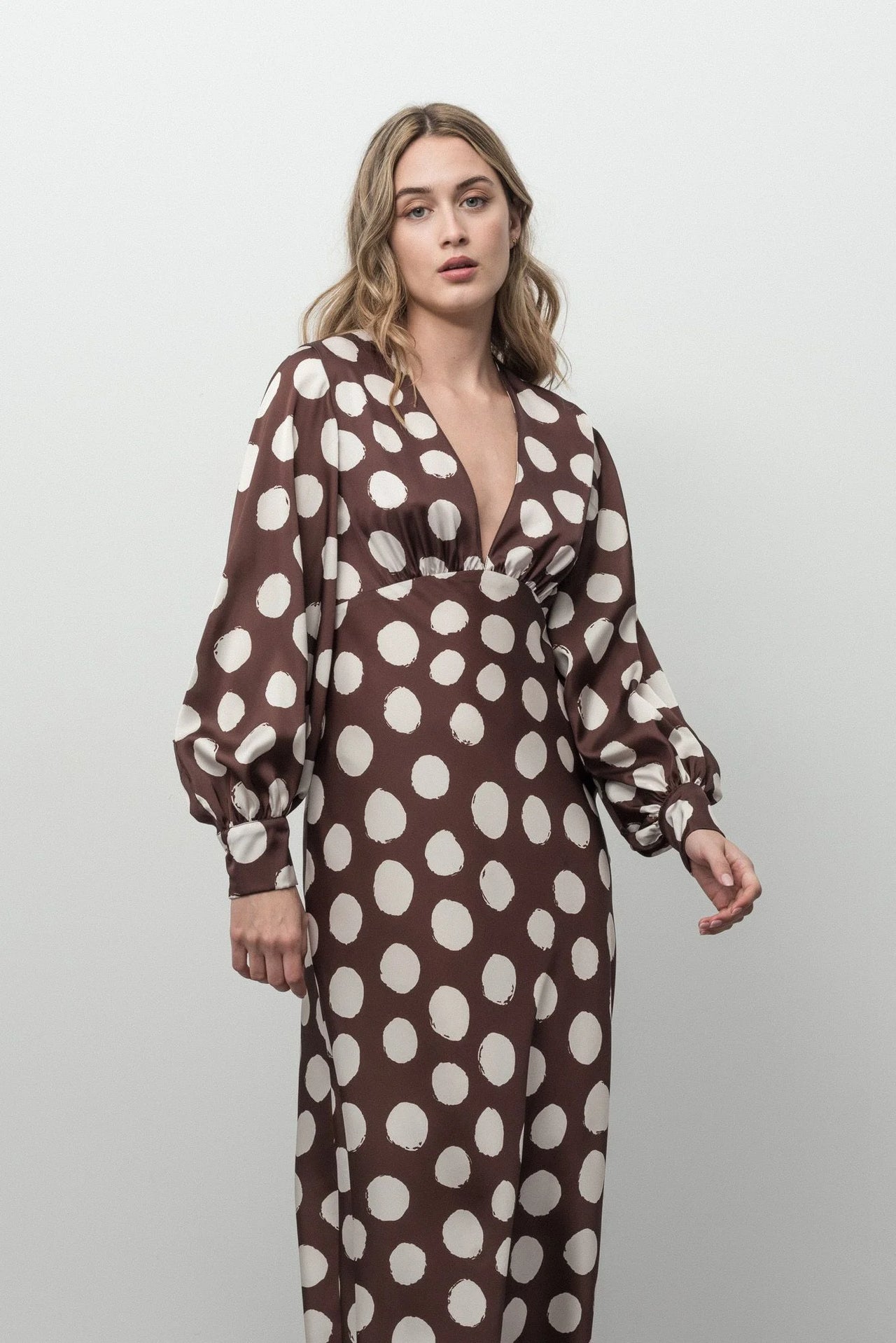 Détail de la robe marron à pois blancs avec décolleté plongeant et manches longues bouffantes, chic et élégante.