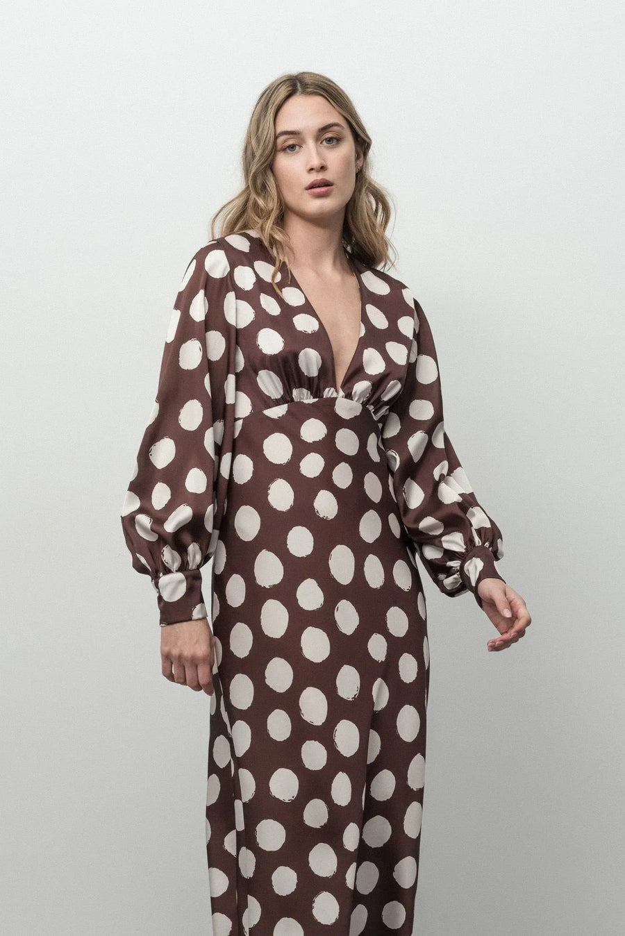 Détail de la robe marron à pois blancs avec décolleté plongeant et manches longues bouffantes, chic et élégante.