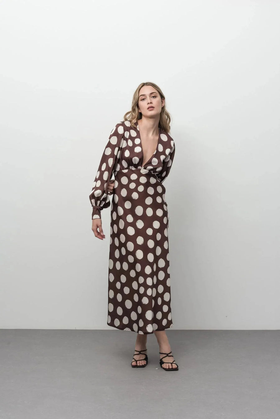 Robe marron à pois blancs midi chic satinée manches longues col V élégante portée par une mannequin, idéale pour des occasions spéciales.