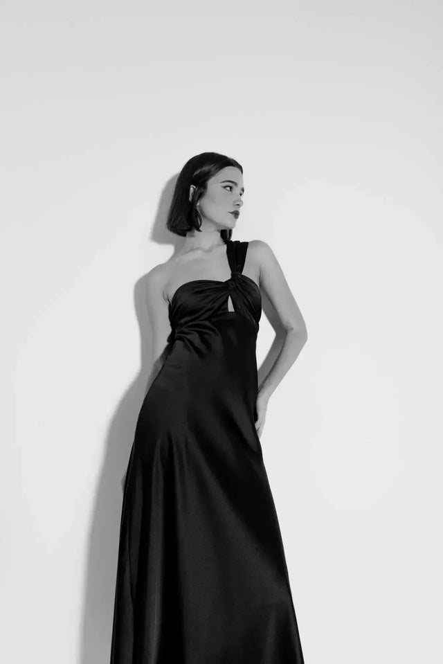 Modèle en noir et blanc portant une robe de soirée femme midi asymétrique noire, mettant en avant le design unique avec encolure sublimante.