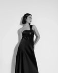 Modèle en noir et blanc portant une robe de soirée femme midi asymétrique noire, mettant en avant le design unique avec encolure sublimante.