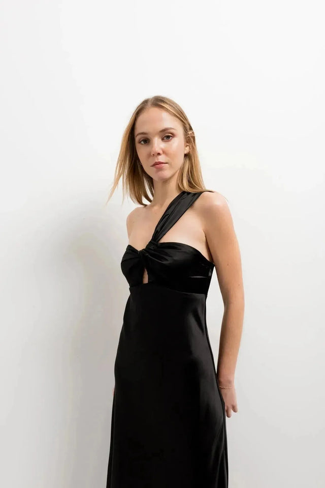 Modèle portant une robe de soirée femme midi asymétrique noire, design unique avec encolure sublimante, mettant en valeur silhouette et élégance.