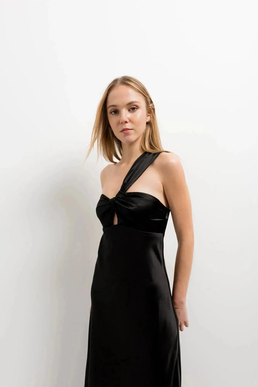 Modèle portant une robe de soirée femme midi asymétrique noire, design unique avec encolure sublimante, mettant en valeur silhouette et élégance.