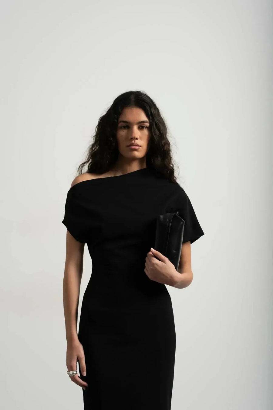 Détail de la robe asymétrique mi longue noire femme, élégance versatile pour soirées tendance 2024. Vue rapprochée du décolleté asymétrique, modèle chic et moderne.