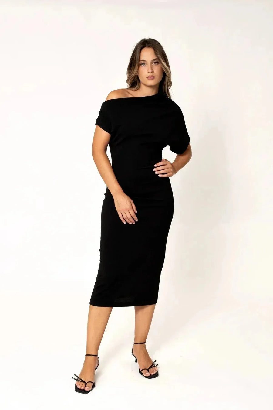 Robe asymétrique mi longue noire femme, élégance versatile pour soirées tendance 2024. Modèle féminin posant avec assurance, mettant en valeur la robe en noir élégant.