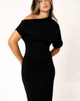 Robe asymétrique mi longue noire femme, élégance versatile pour soirées tendance 2024. Présentation d'une femme regardant légèrement sur le côté, mettant en avant la coupe élégante.