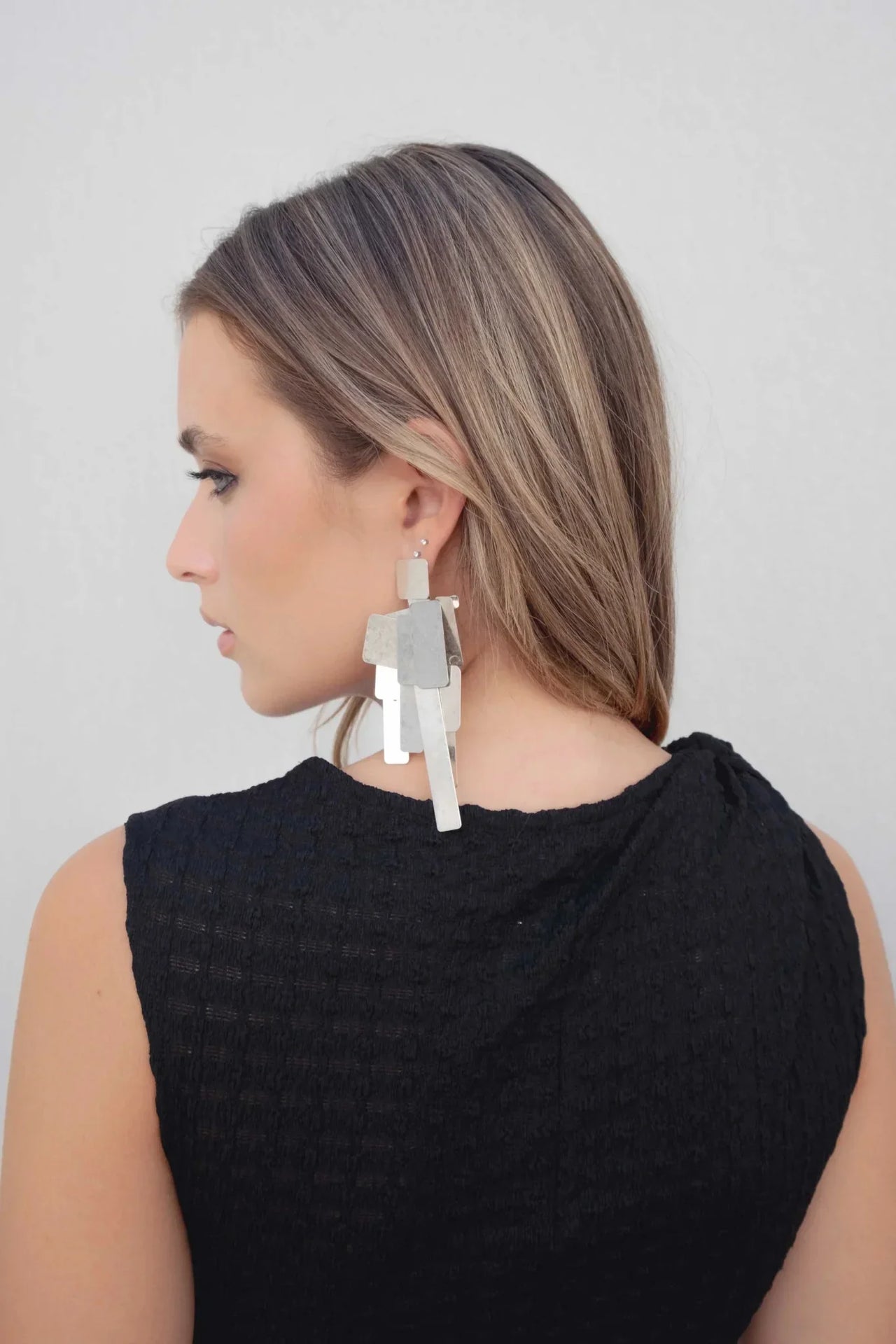 Femme montrant sa coiffure et le détail de sa robe maille noire asymétrique moulante avec détail noué à une épaule – longueur midi, accent sur les accessoires.