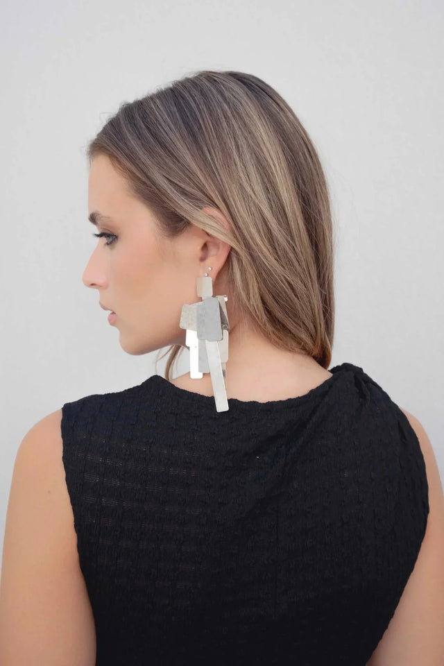 Femme montrant sa coiffure et le détail de sa robe maille noire asymétrique moulante avec détail noué à une épaule – longueur midi, accent sur les accessoires.