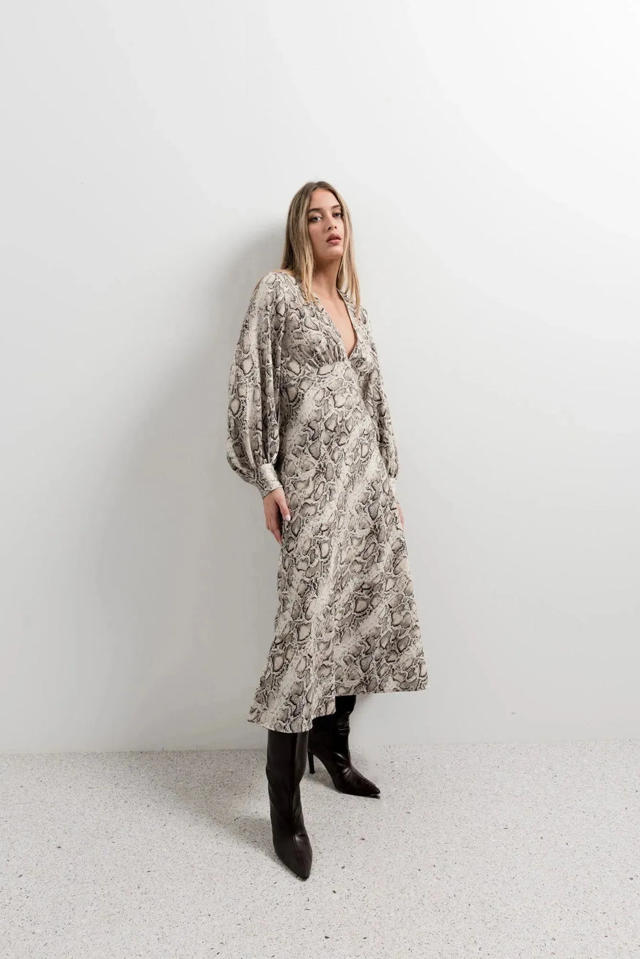 Modèle avec une robe midi imprimé python à col cache-cœur, posant avec style. La coupe fluide et les manches bouffantes soulignent l’élégance de cette robe animal.