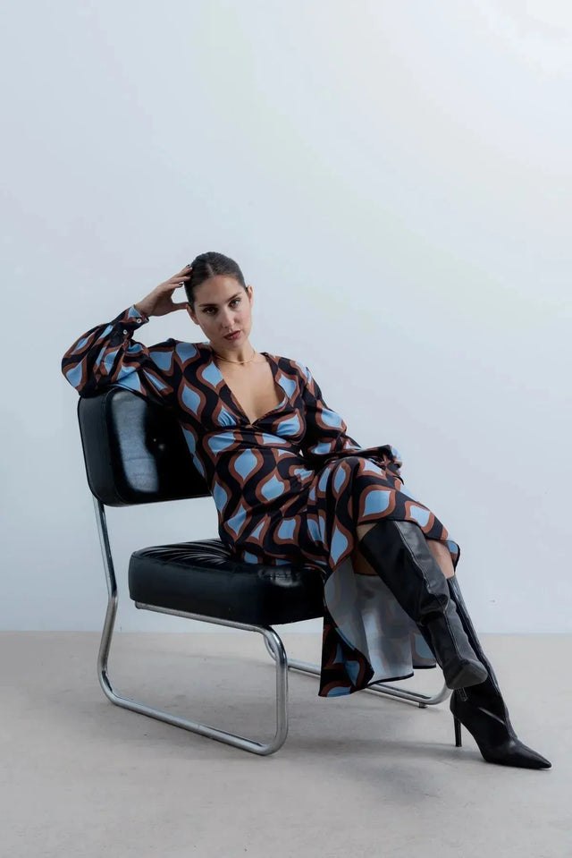 Femme posant dans une robe motif géométrique midi à décolleté profond et manches bouffantes, combinant élégance et audace.