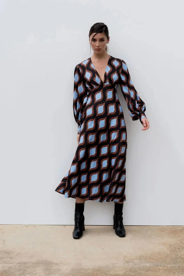 Femme assise dans une robe motif géométrique midi avec décolleté V et manches bouffantes, apportant une touche de style vintage à son look.