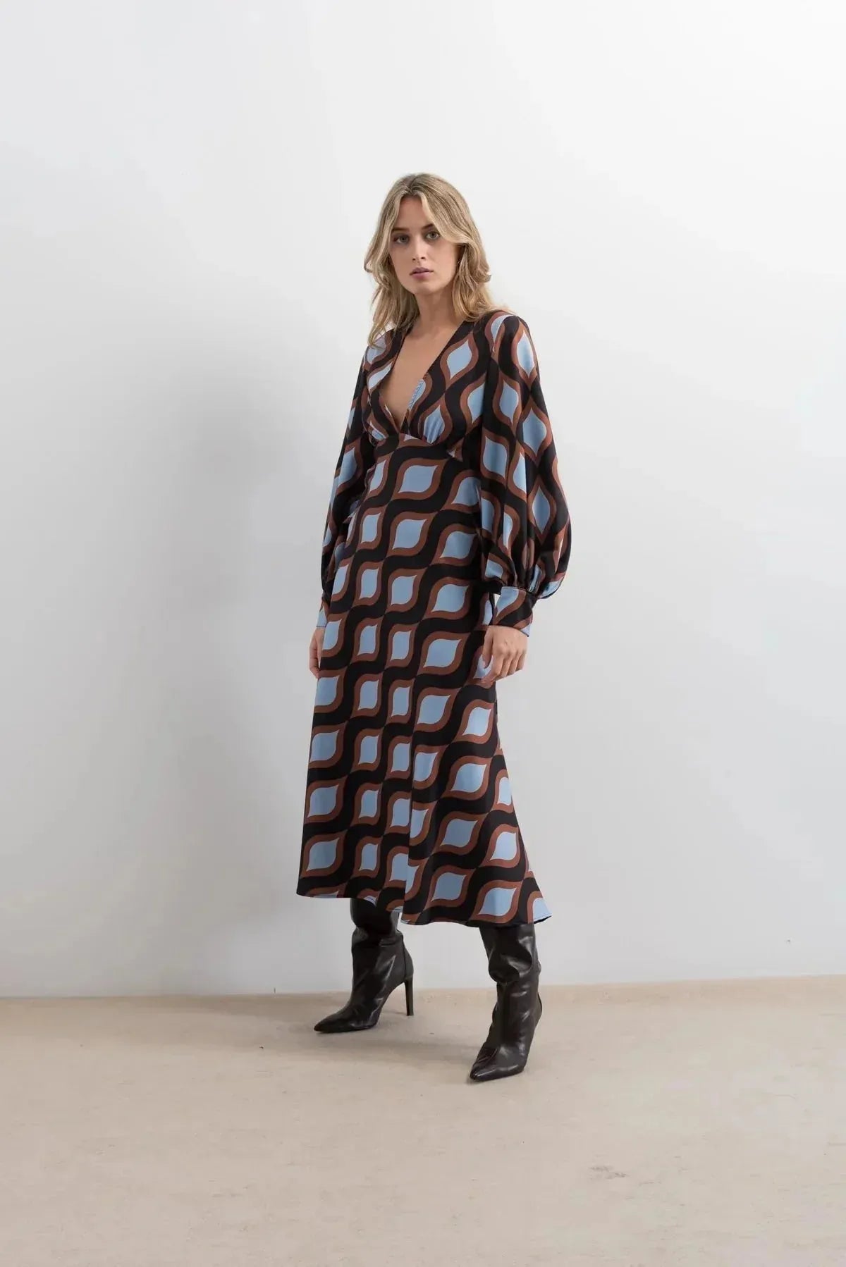 Femme stylée dans une robe motif géométrique midi avec décolleté V profond et manches longues bouffantes, affichant un look élégant et raffiné.