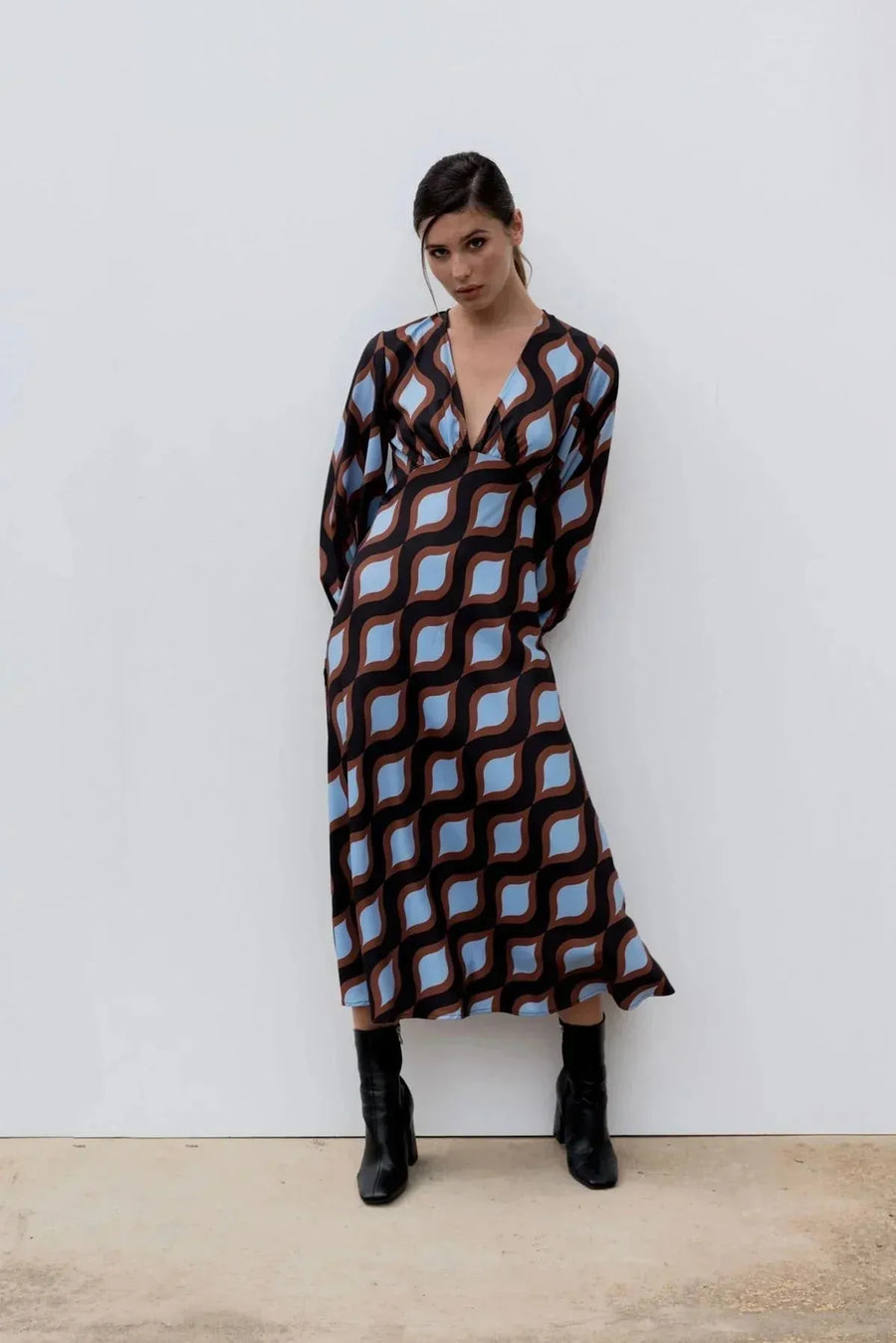 Femme dans une robe motif géométrique midi avec décolleté en V profond, mettant en avant le motif original des couleurs marron, bleu et noir.