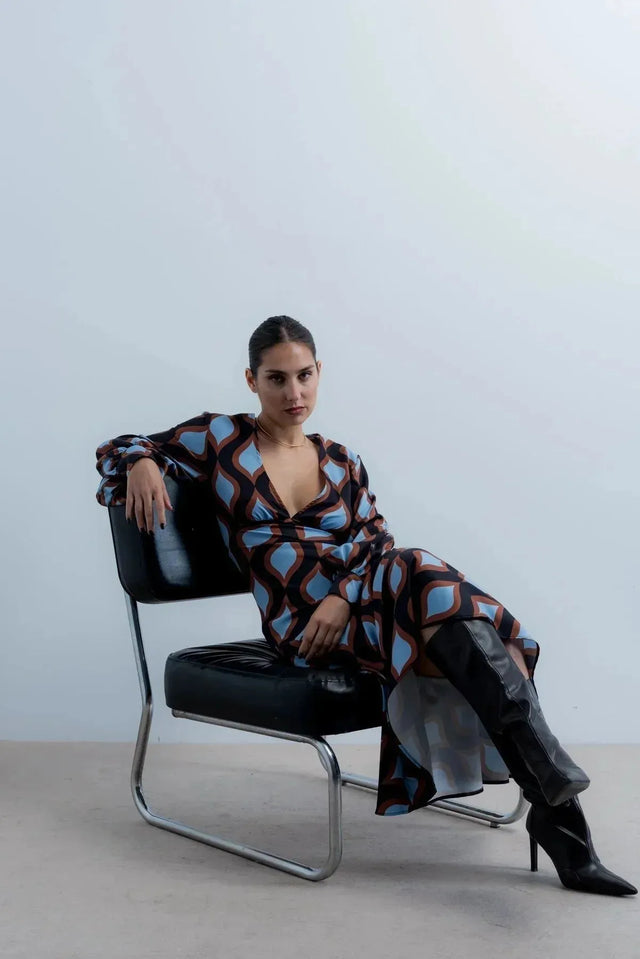 Femme assise dans une robe motif géométrique midi à décolleté profond, illustrant son style tendance et original.