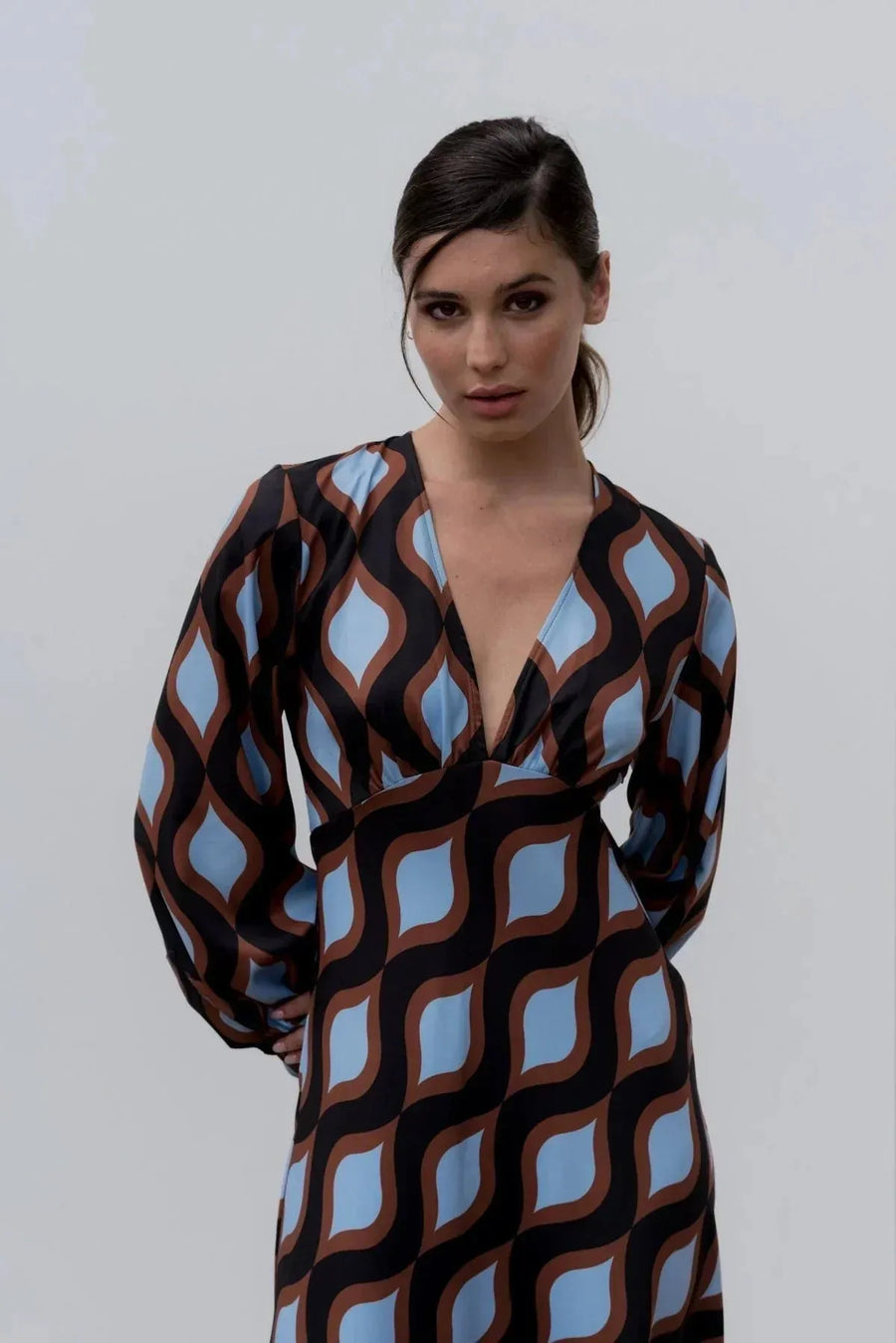 Femme posant dans une robe motif géométrique midi au décolleté V profond et aux manches bouffantes, soulignant son style unique et vibrant.