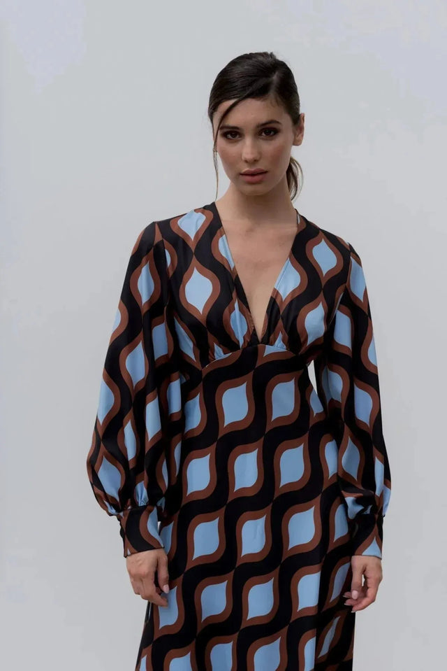 Modèle portant une robe motif géométrique midi avec décolleté V profond et manches longues bouffantes, mettant en valeur le motif ondulé marron et bleu.
