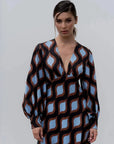 Modèle portant une robe motif géométrique midi avec décolleté V profond et manches longues bouffantes, mettant en valeur le motif ondulé marron et bleu.