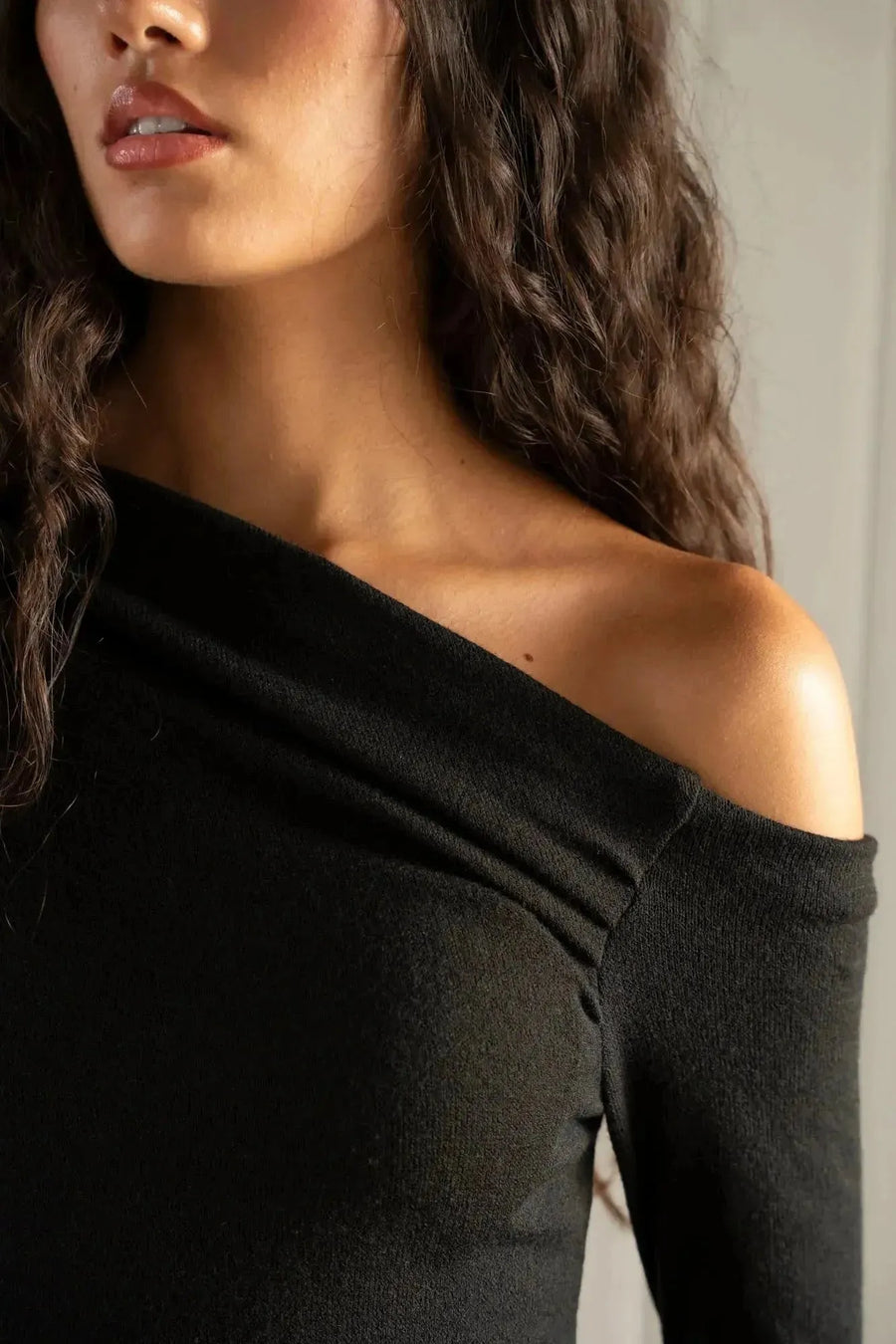 Détail de la robe midi noire à coupe asymétrique, soulignant l'aspect intemporel et confortable de la robe maille.