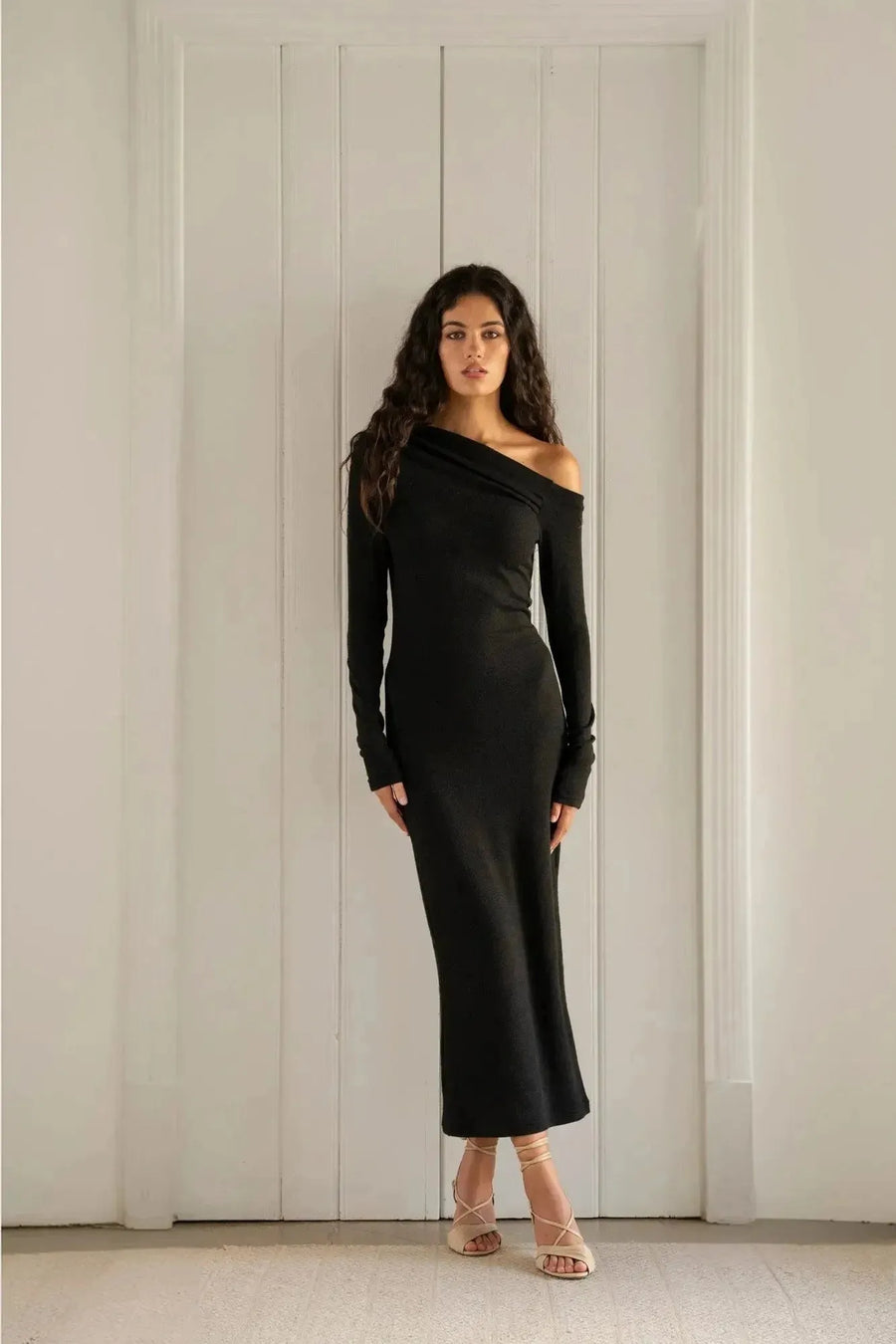 Femme portant une robe midi noire à coupe asymétrique, mettant en valeur la robe maille avec des détails élégants et une silhouette flatteuse.