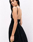 Modèle montrant le dos de la robe midi noire à fines bretelles, révélant le design smocké et fluide. Parfaite comme robe noire longue dos nu pour l'été.